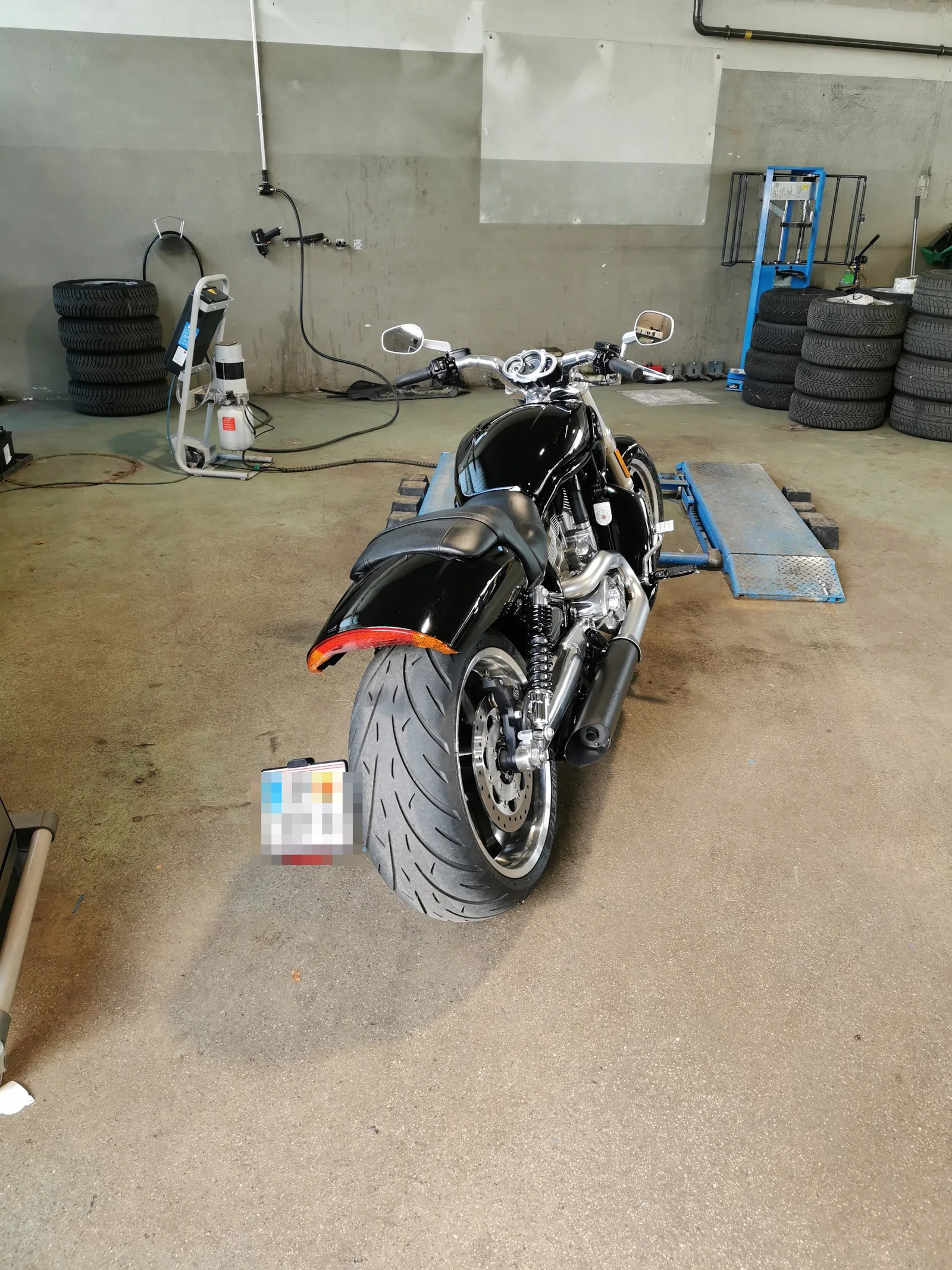 Motorrad von hinten auf der Motorrad-Hebebühne, rechts und links Stapel mit eingelagerten Reifen